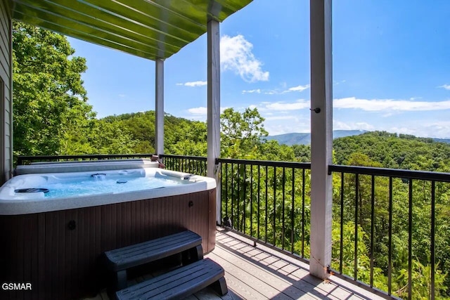 deck with a mountain view, a hot tub, and a view of trees