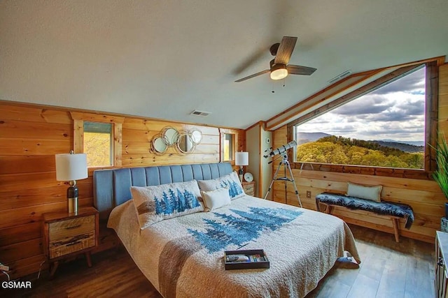 bedroom with vaulted ceiling, wooden walls, visible vents, and wood finished floors