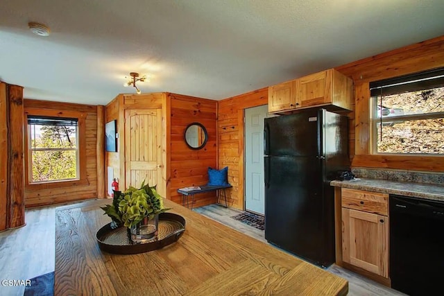 kitchen with light wood-type flooring, dark countertops, black appliances, and wood walls