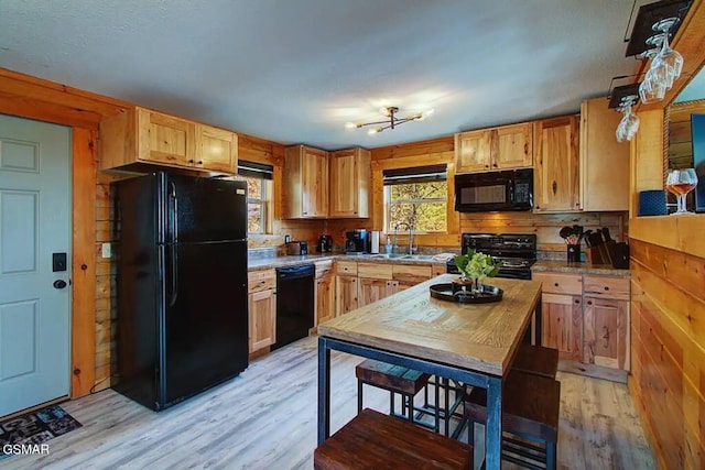 kitchen featuring a sink, black appliances, light wood-style flooring, and wood walls