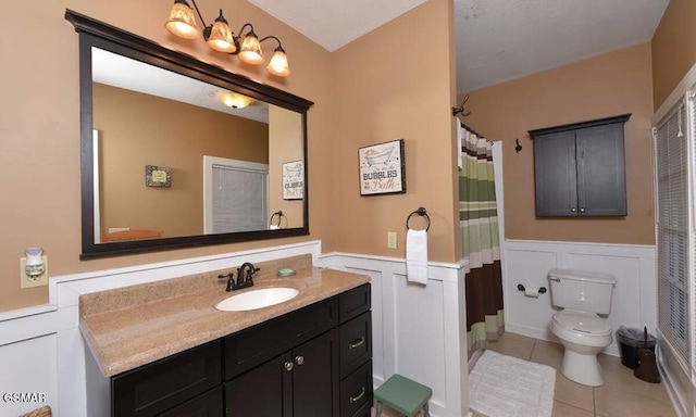 bathroom featuring curtained shower, toilet, wainscoting, vanity, and tile patterned floors