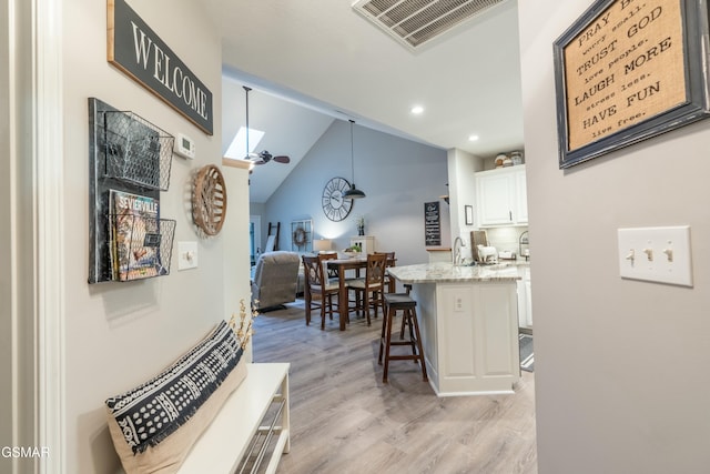 kitchen featuring a breakfast bar, lofted ceiling with skylight, light stone counters, white cabinets, and light wood-type flooring