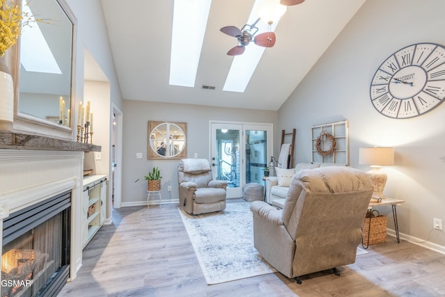 living room featuring a skylight, high vaulted ceiling, ceiling fan, and light hardwood / wood-style flooring