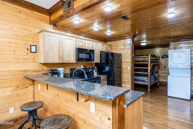 415 Big Bear Way, Pigeon Forge, TN 37863 - kitchen with stacked washing machine and dryer, black appliances, wood walls, light wood-type flooring, and a breakfast bar