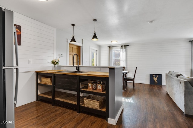 kitchen featuring wood walls, stainless steel fridge, dark hardwood / wood-style flooring, and sink