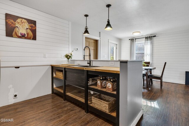 kitchen with kitchen peninsula, sink, dark hardwood / wood-style floors, hanging light fixtures, and wood walls