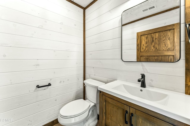 bathroom with toilet, wood walls, and vanity