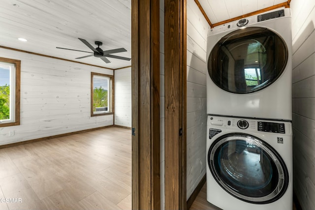 laundry area with ceiling fan, laundry area, wood walls, stacked washer and dryer, and wood finished floors