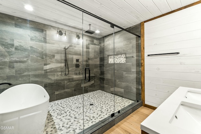 bathroom with recessed lighting, a shower stall, double vanity, a freestanding bath, and wood finished floors