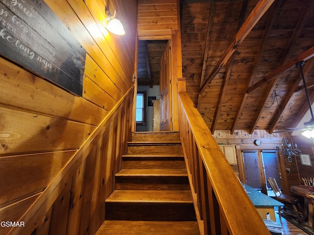 stairway with vaulted ceiling with beams, wooden walls, and wooden ceiling