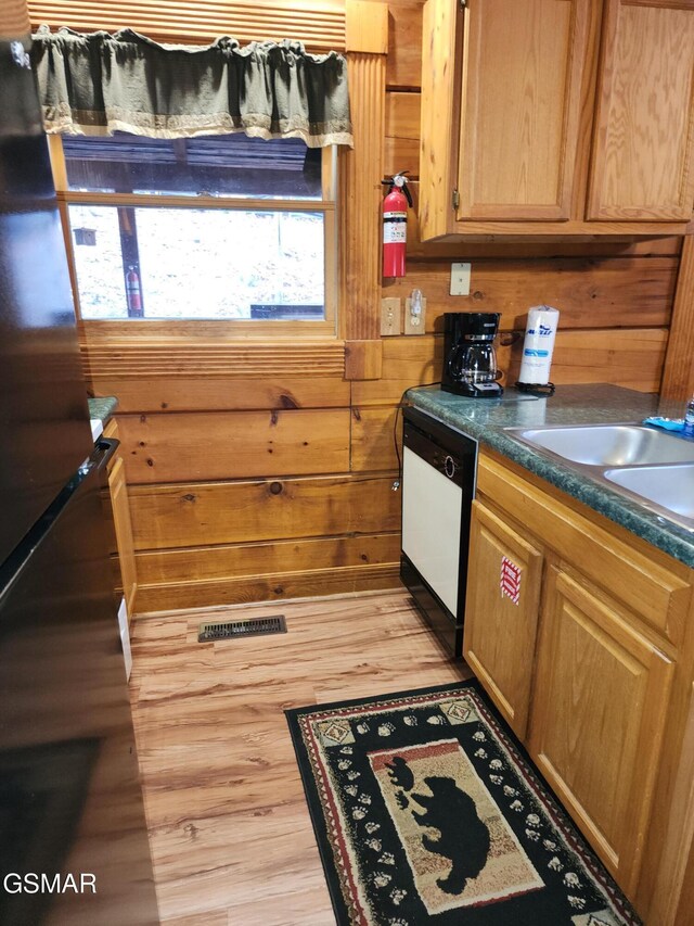 kitchen featuring light wood-type flooring, white dishwasher, wooden walls, and sink