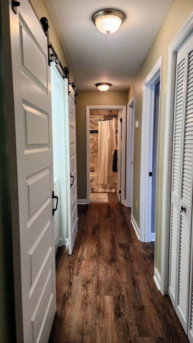 hallway with baseboards, dark wood-style floors, and a barn door