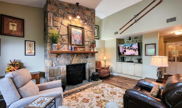 living area featuring visible vents, a stone fireplace, high vaulted ceiling, and wood finished floors