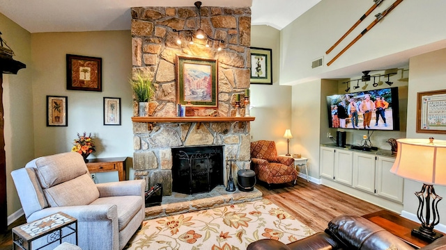 living room featuring visible vents, a fireplace, vaulted ceiling, wood finished floors, and baseboards