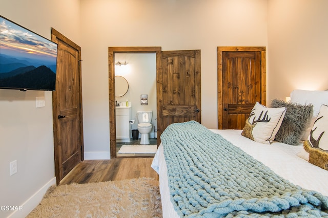bedroom featuring baseboards, ensuite bath, and wood finished floors