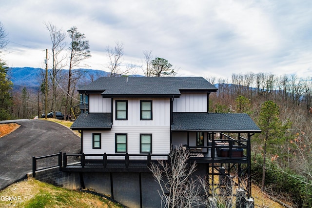 back of house with board and batten siding, roof with shingles, and a deck with mountain view