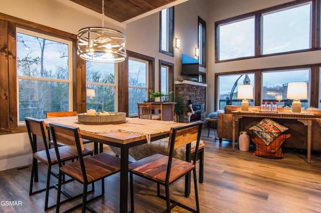 dining area with a towering ceiling, wood finished floors, a notable chandelier, and a stone fireplace