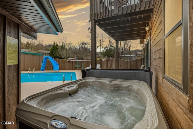 pool at dusk featuring a hot tub and a water slide