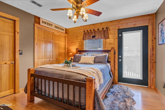 bedroom featuring light hardwood / wood-style flooring, a closet, ceiling fan, and wood walls