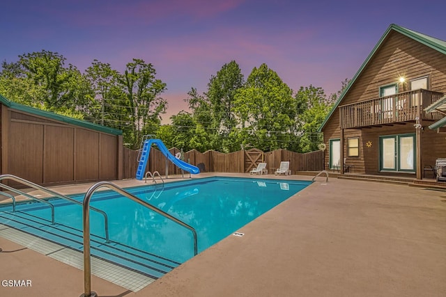 pool at dusk with a water slide and a patio area