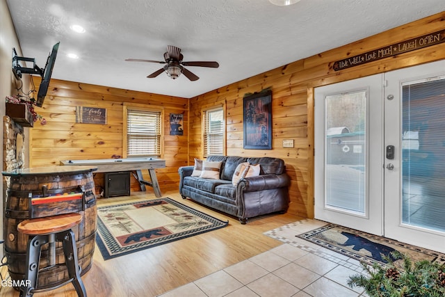 living room featuring ceiling fan, light tile patterned floors, a textured ceiling, and wood walls