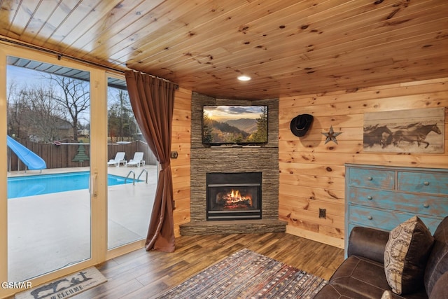 living room with hardwood / wood-style flooring, wooden ceiling, an outdoor stone fireplace, and wood walls