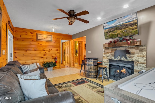 living room featuring ceiling fan, a stone fireplace, and wooden walls