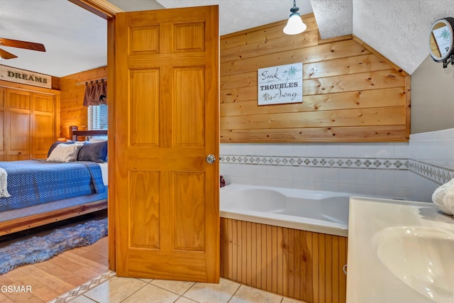 bathroom featuring sink, ceiling fan, a textured ceiling, a bathing tub, and wood walls