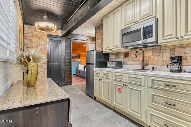 kitchen featuring appliances with stainless steel finishes, cream cabinets, sink, decorative backsplash, and a barn door