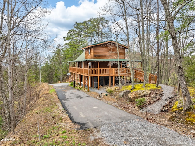 view of front of home with aphalt driveway, a deck, metal roof, and log veneer siding