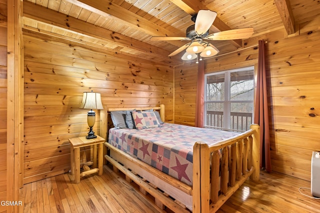 bedroom featuring a ceiling fan, wood walls, beam ceiling, light wood finished floors, and wooden ceiling
