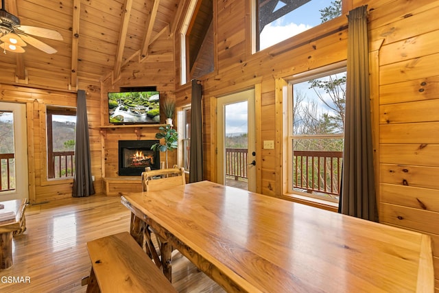 dining room featuring wooden ceiling, wood walls, beamed ceiling, and a warm lit fireplace