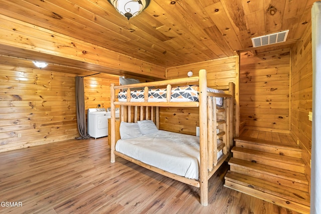 bedroom featuring wood finished floors, wood walls, visible vents, and washer and clothes dryer