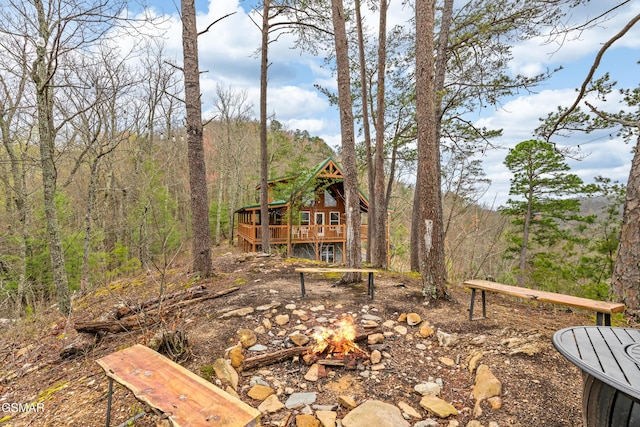 view of yard with a wooded view, a wooden deck, and a fire pit