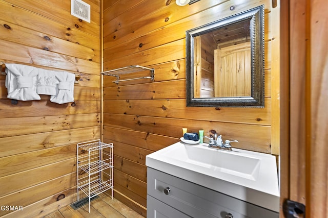 bathroom featuring wood walls, wood finished floors, vanity, and visible vents