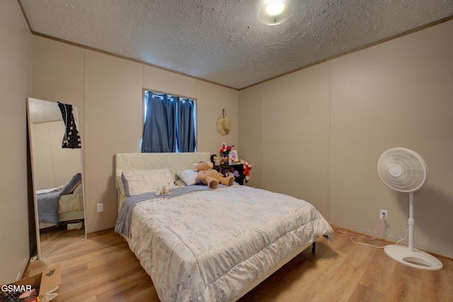 bedroom featuring wood finished floors, a textured ceiling, a decorative wall, and crown molding