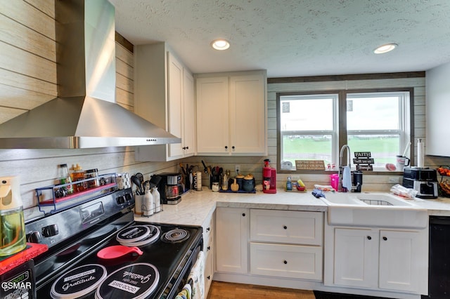 kitchen with electric range oven, wall chimney range hood, a sink, a textured ceiling, and black dishwasher