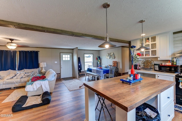 kitchen featuring a textured ceiling, wooden counters, open floor plan, white cabinets, and wood finished floors