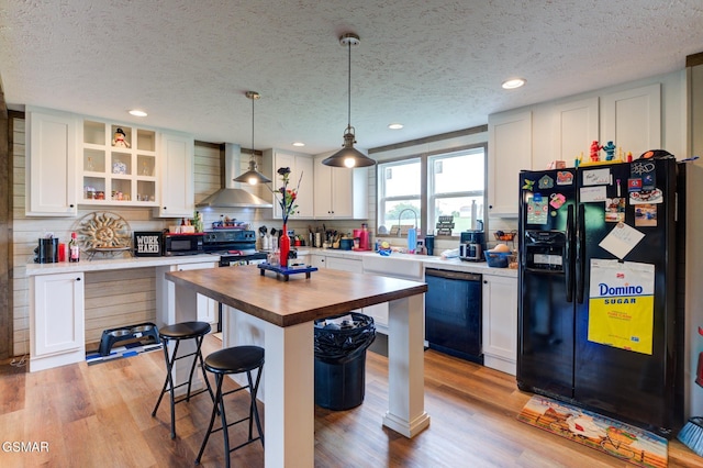 kitchen featuring black appliances, wall chimney exhaust hood, wood counters, a kitchen breakfast bar, and open shelves