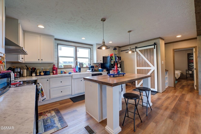 kitchen featuring a barn door, butcher block counters, black appliances, a breakfast bar area, and white cabinetry