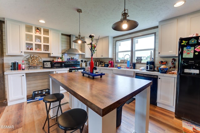 kitchen featuring black appliances, wall chimney exhaust hood, butcher block countertops, a textured ceiling, and open shelves
