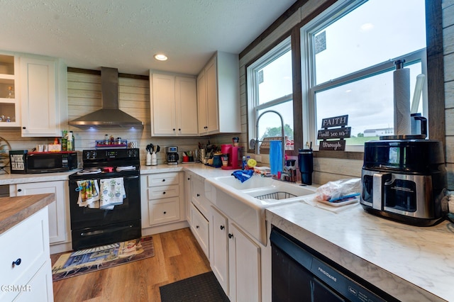 kitchen featuring black appliances, wall chimney range hood, white cabinets, a textured ceiling, and recessed lighting