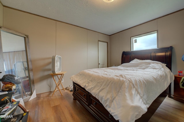 bedroom with ornamental molding, light wood finished floors, and a textured ceiling