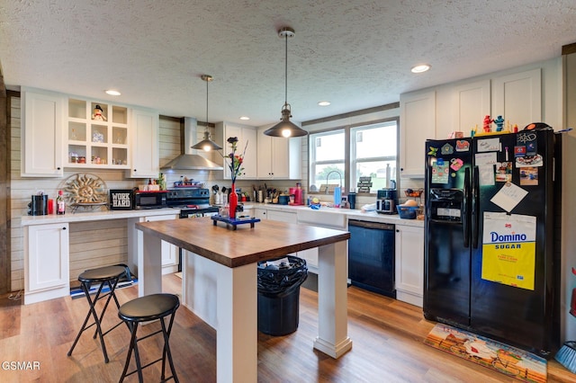 kitchen with black appliances, wall chimney exhaust hood, wooden counters, a kitchen breakfast bar, and open shelves