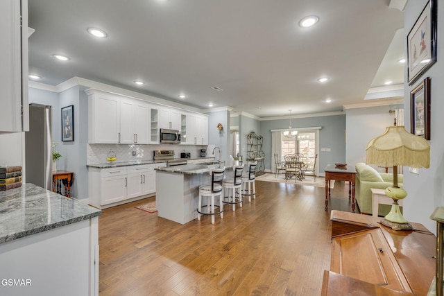 kitchen featuring a breakfast bar area, stone counters, stainless steel appliances, white cabinetry, and a center island with sink