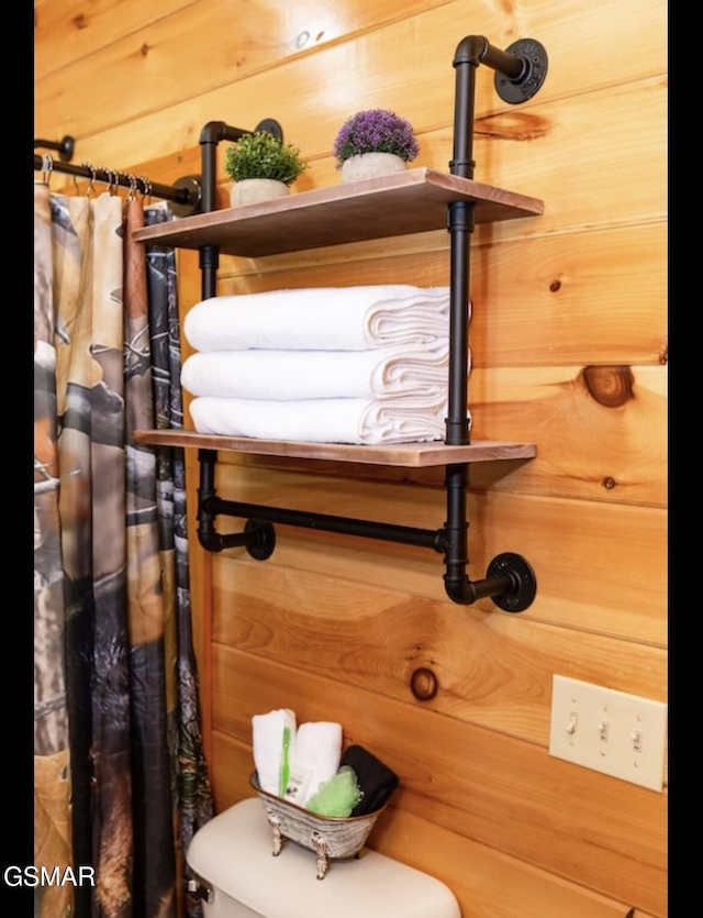 details featuring a shower with shower curtain, toilet, and wooden walls