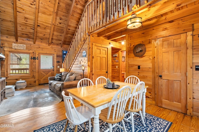 dining space with beamed ceiling, stairway, wood-type flooring, wooden walls, and wooden ceiling