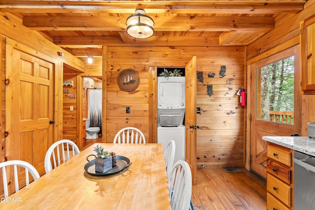 dining area featuring light wood-type flooring, beamed ceiling, wooden walls, and stacked washer and clothes dryer