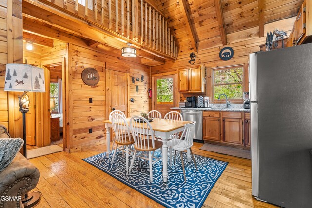 dining area featuring beam ceiling, wooden walls, light wood-style flooring, and wooden ceiling