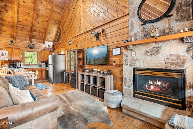 living area featuring beamed ceiling, light wood-style flooring, wooden walls, a fireplace, and wood ceiling